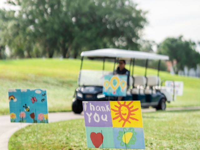 Golf cart in background, with a forefront sign made by a child, saying thank you.